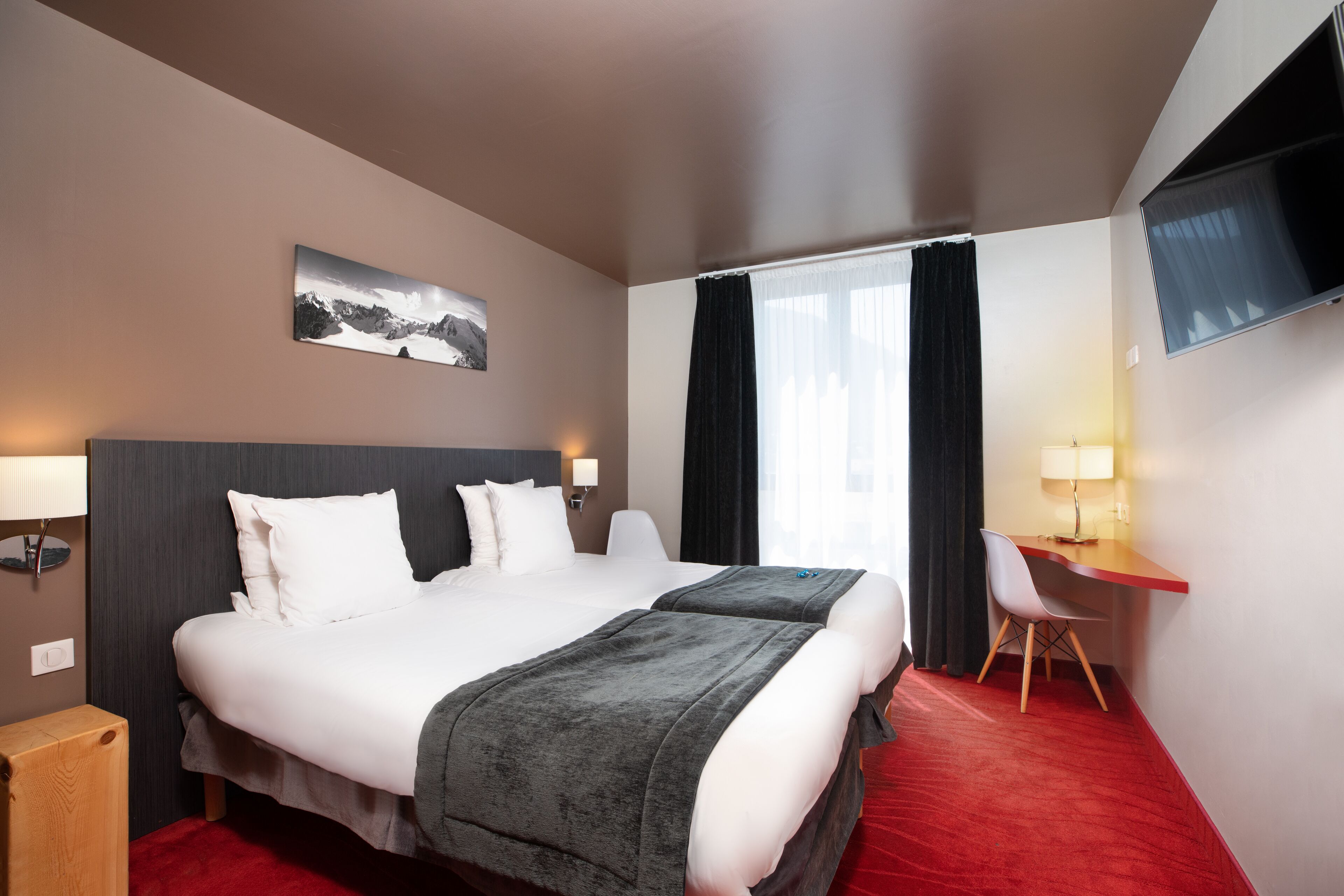 A hotel room with two beds, a desk, a chair, a TV, and a painting on the wall.