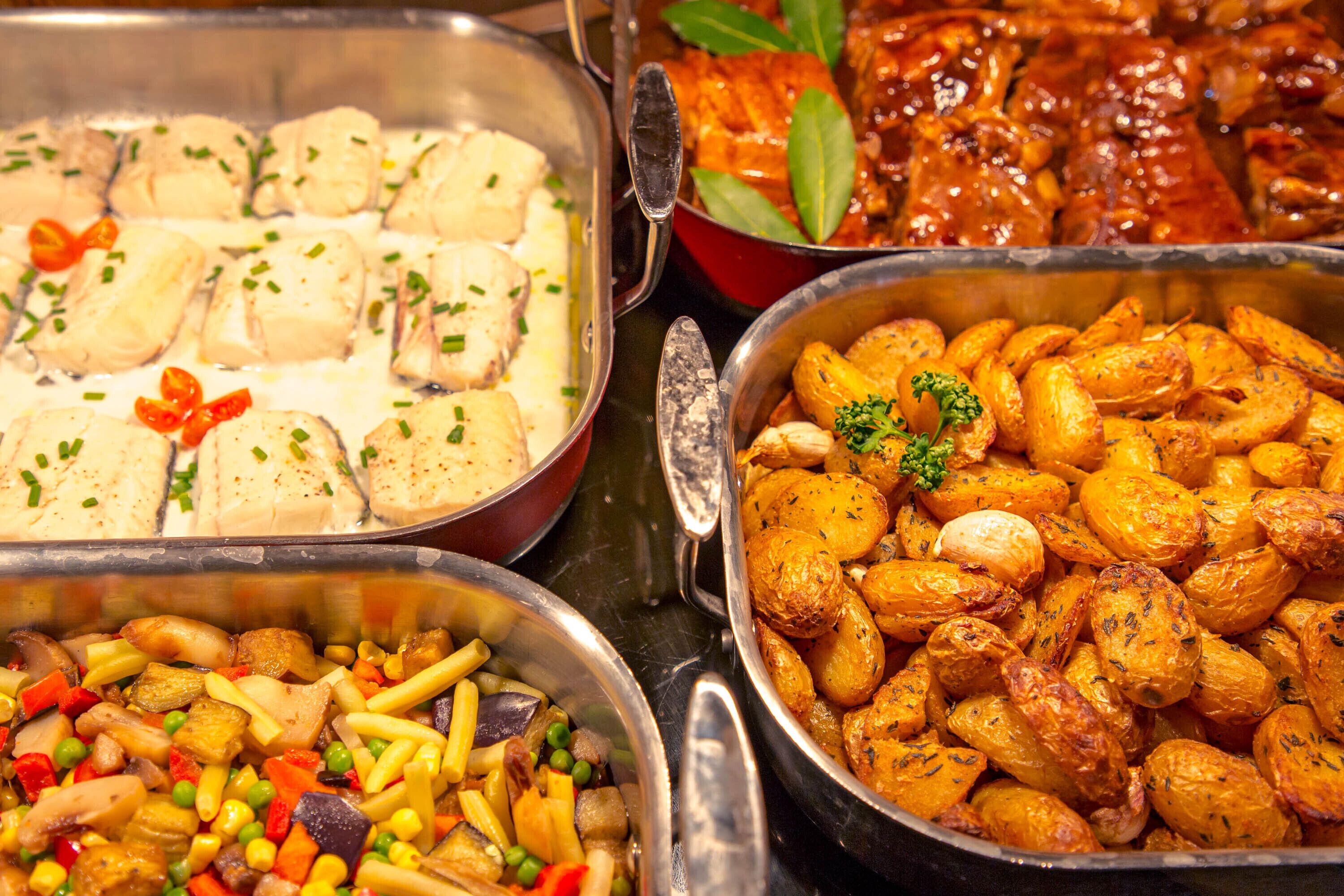 A buffet with various dishes including fish, roasted potatoes, and mixed vegetables.