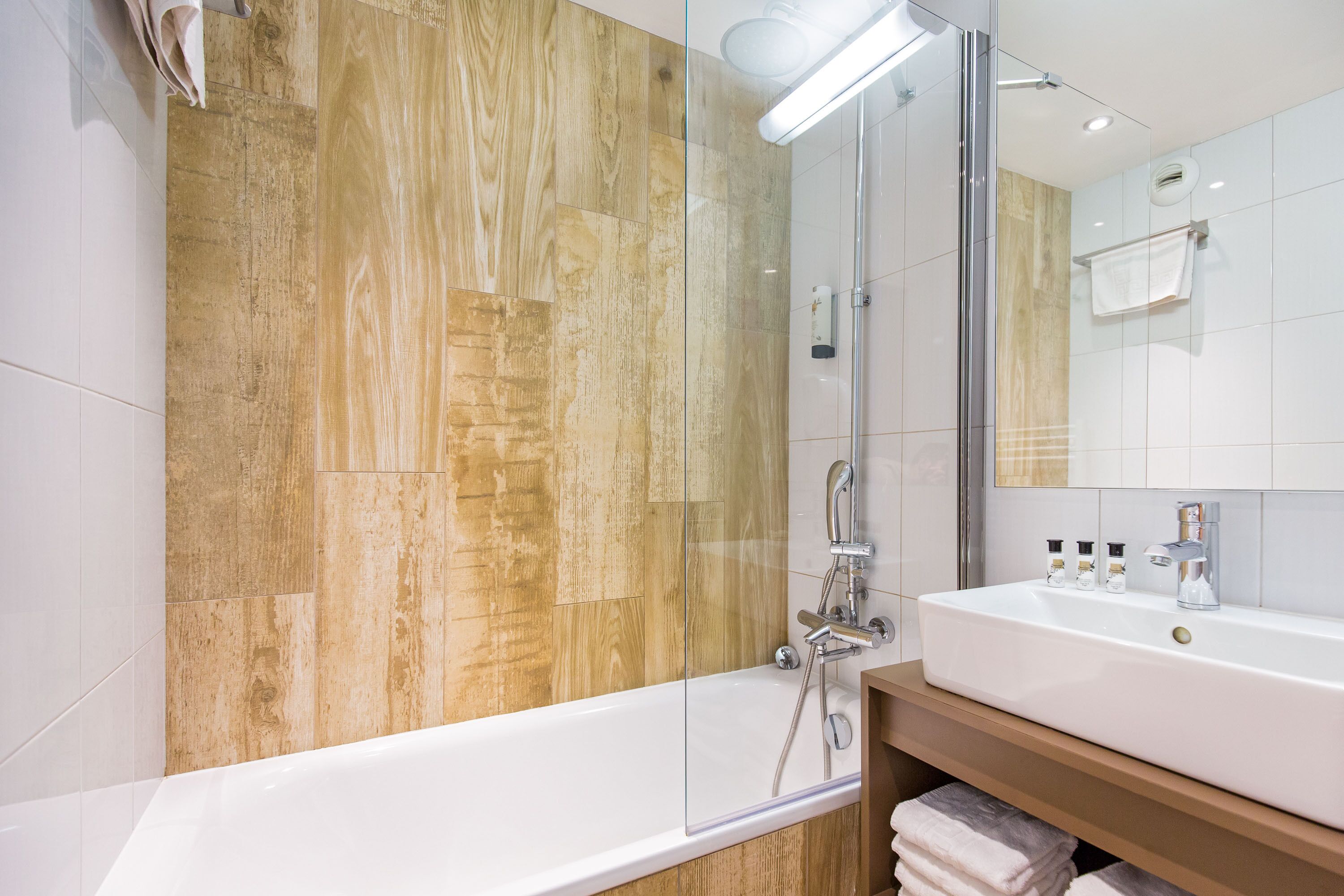 Un baño moderno con ducha envuelta en vidrio, un lavabo blanco y paneles de madera en las paredes.