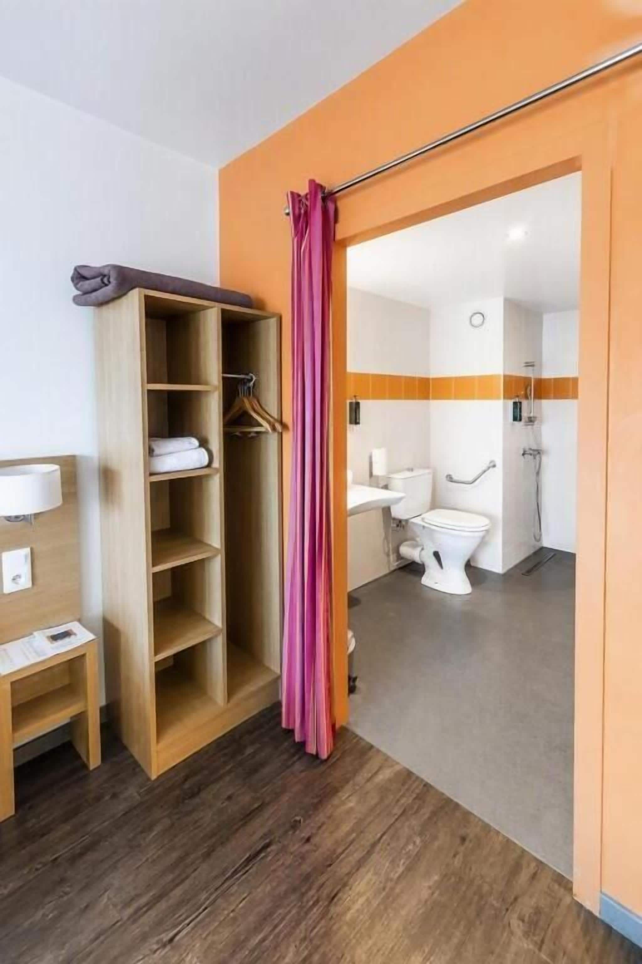 A hotel bathroom with a wooden wardrobe, a shower curtain, and a toilet.