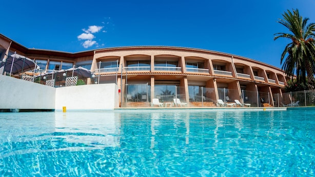 A hotel with a pool, multiple balconies, and sun loungers.