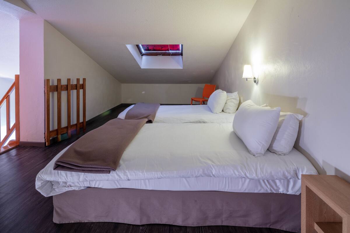 Une chambre avec deux lits, une lucarne, une chaise en bois et une table de chevet.