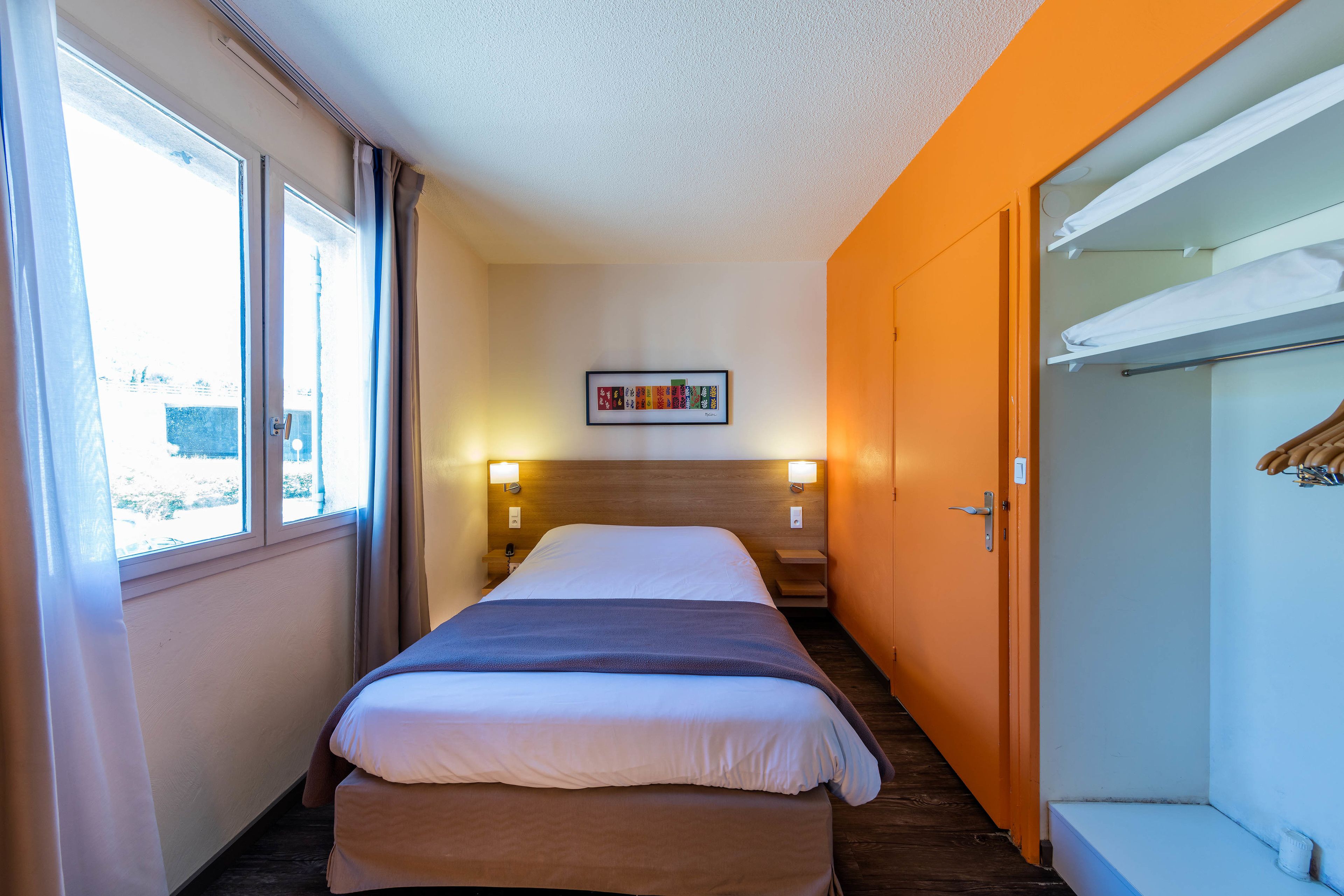 A hotel room with a bed, bedside lamps, a window, and a wardrobe.