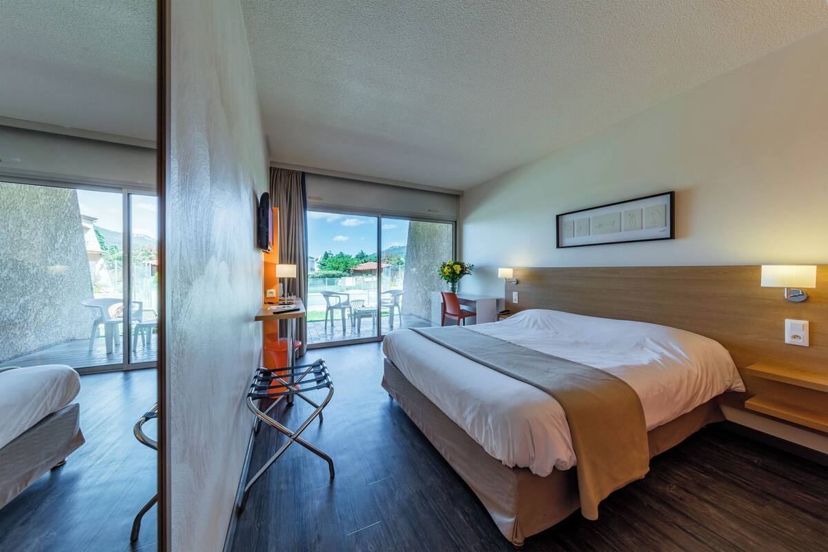 Une chambre d’hôtel avec un lit, un bureau, une chaise et une vue sur l’extérieur.