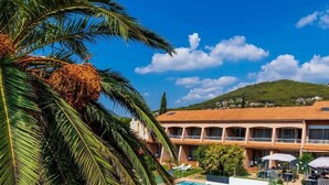 A hotel with a pool, palm trees, and a mountain in the background.
