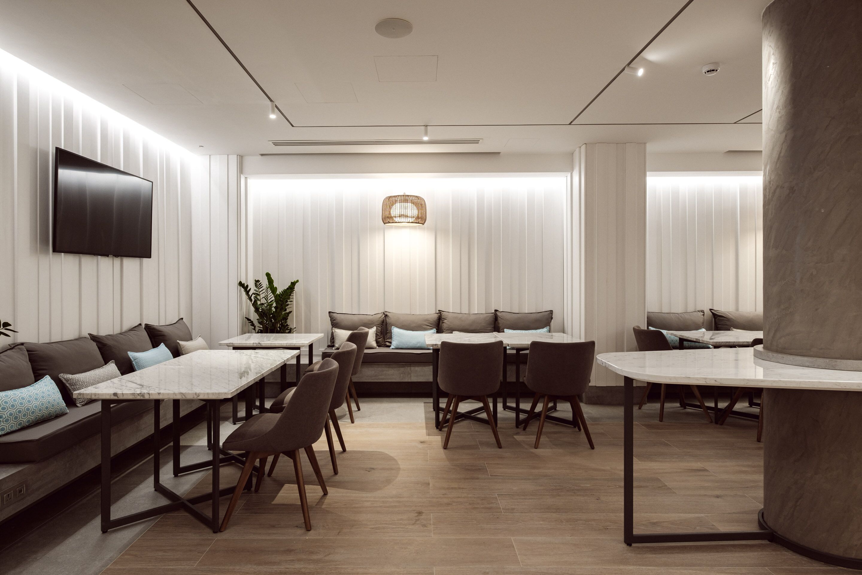 A modern dining area with a long table, several chairs, a sofa, and a TV mounted on the wall.
