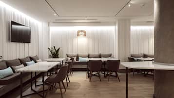 A modern dining area with a long table, several chairs, a sofa, and a TV mounted on the wall.
