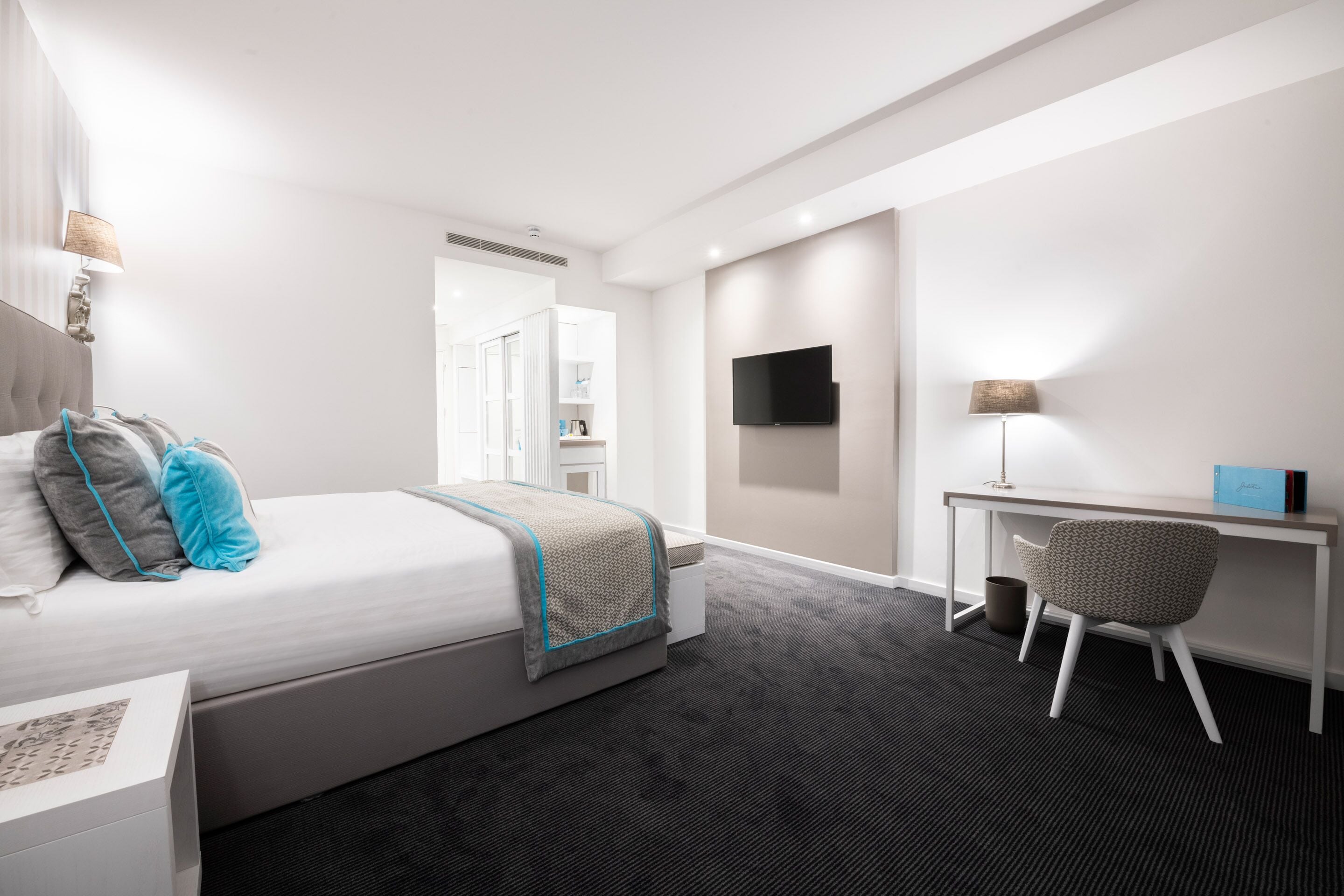 Una camera d'albergo moderna con un letto, una scrivania, una sedia e una televisione a schermo piatto appesa al muro.