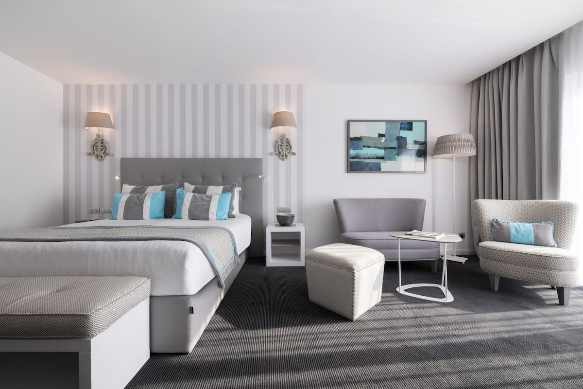 Ein modernes Hotelzimmer mit einem großen Bett, einem grauen Sessel, einem kleinen Tisch und einer Couch.
