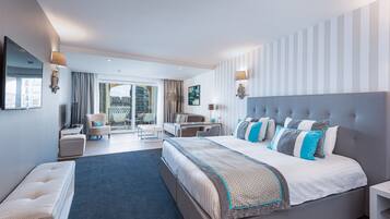 Ein modernes Hotelzimmer mit einem großen Bett, einer Sitzecke mit einer Couch und Sesseln, einem Esstisch und einem Balkon mit Blick auf die Stadt.