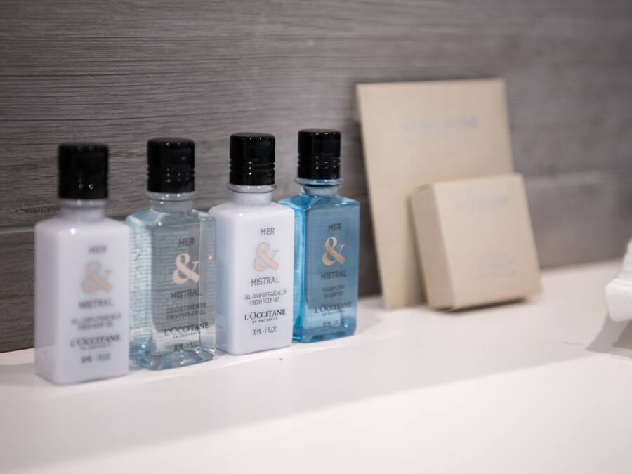 Una encimera de baño con cuatro botellas de gel de ducha Mistral, una toalla blanca y una caja color beige.