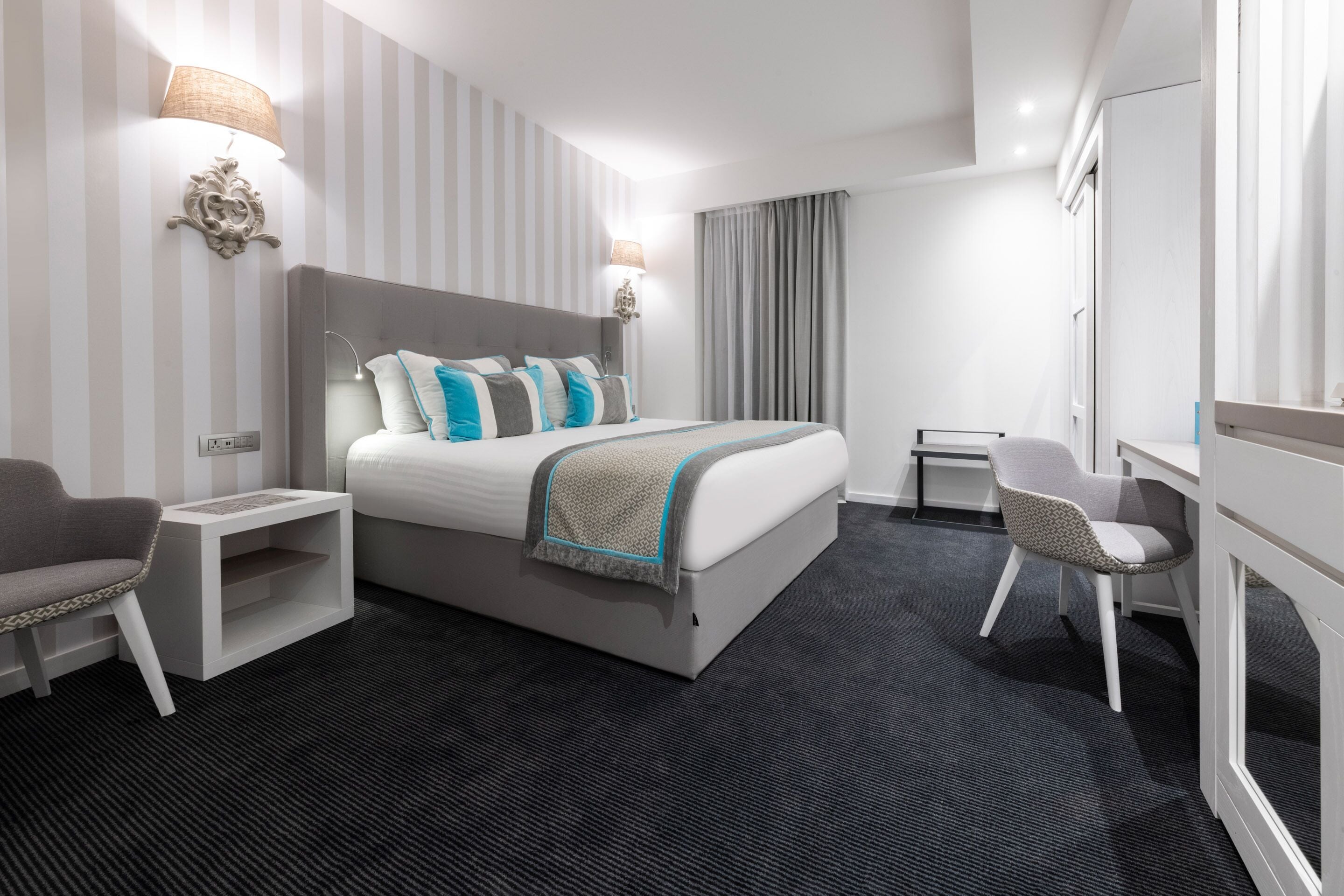 A modern hotel room with a large bed, bedside tables, a desk, and a chair.