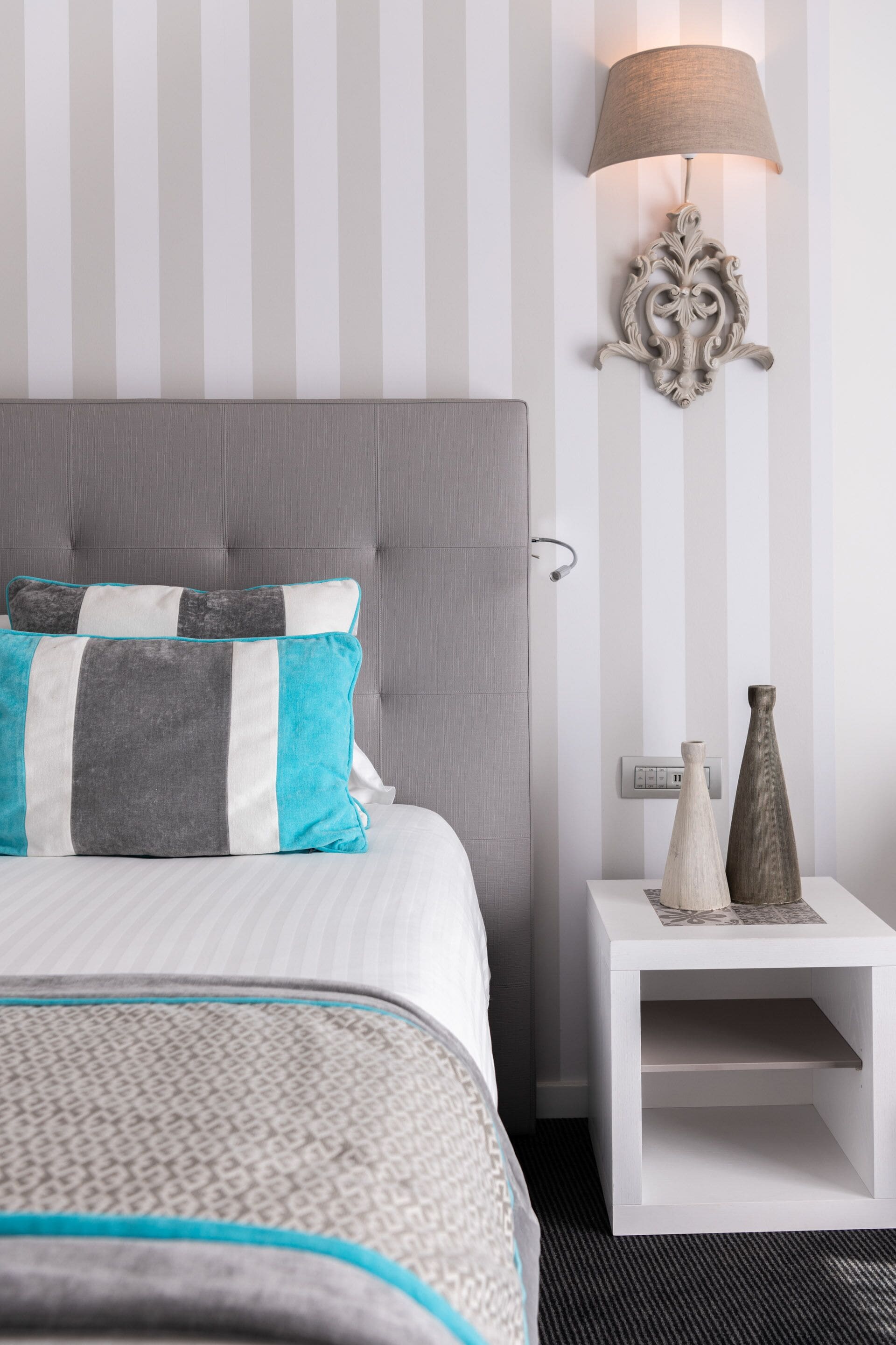 A neatly arranged hotel room with a bed, a bedside lamp, and a nightstand with decorative items.