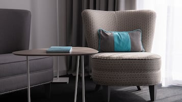 Ein modernes Zimmer mit einem grauen Sofa, einem gemusterten Sessel mit einem türkisfarbenen Kissen und einem kleinen runden Tisch mit einem Buch.