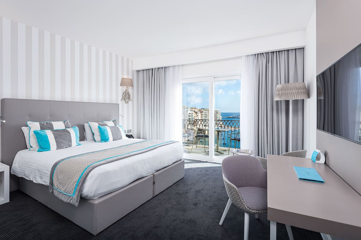 Ein Hotelzimmer mit einem großen Bett, einem Schreibtisch und Blick auf die Stadt.