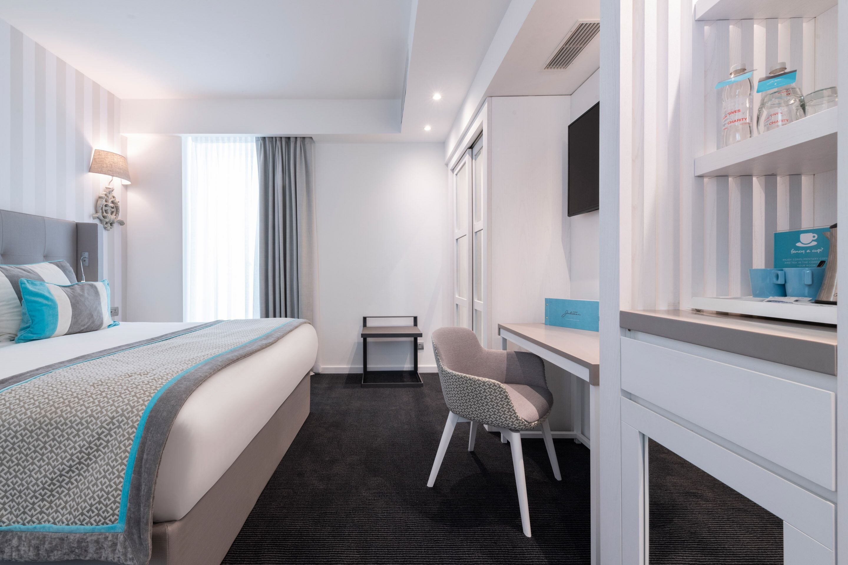 Ein Hotelzimmer mit Bett, Schreibtisch, Stuhl, Fernseher und einer Ablage mit Gläsern.
