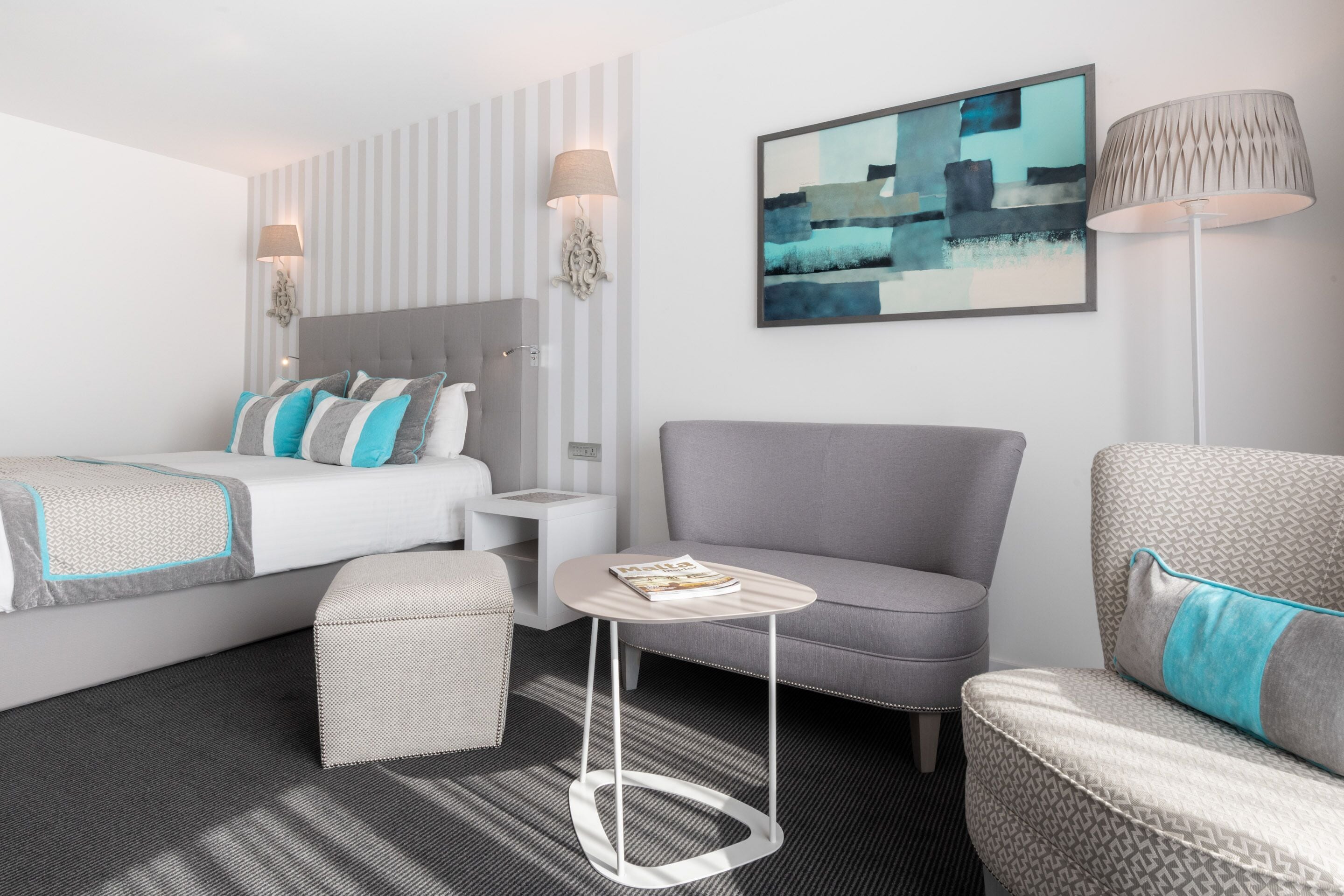 Une chambre d’hôtel moderne, équipée d’un lit, de deux fauteuils, d’une petite table et d’une lampe.