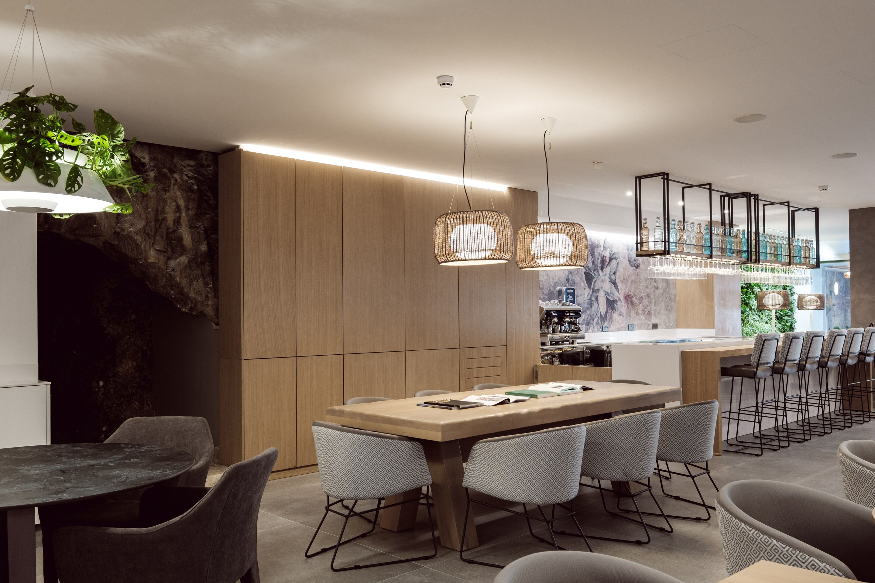 A modern kitchen with wooden cabinets, a central island with bar stools, pendant lighting, and a hanging plant.