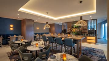 Un restaurante moderno con mesas redondas, sillas azules e iluminación colgante.