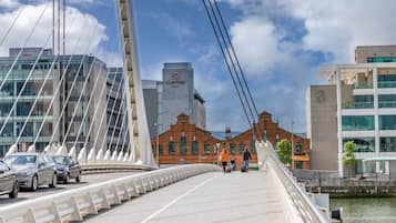 Uma ponte para pedestres com design moderno, um Hotel Clayton e um edifício histórico com janelas verdes.