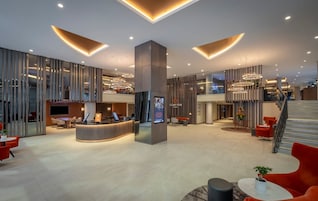 Un moderno vestíbulo de hotel con mostrador de recepción, zonas de estar y una escalera.