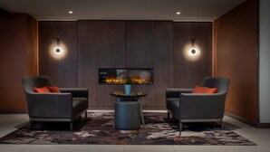 A modern room with two armchairs, a central table, and a television displaying a fireplace. - Clayton Hotel Cardiff Lane (Dublin)
