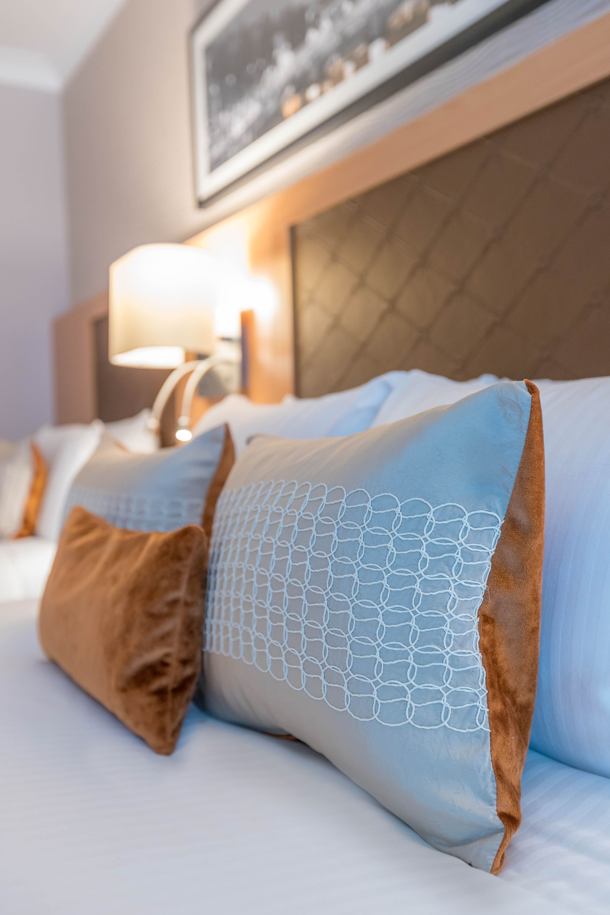 Una habitación de hotel con una cama bien hecha, un cabecero y una lámpara sobre una mesita de noche.