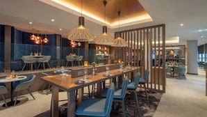 A modern dining area with a long table, blue chairs, and pendant lights. - Clayton Hotel Cardiff Lane (Dublin)