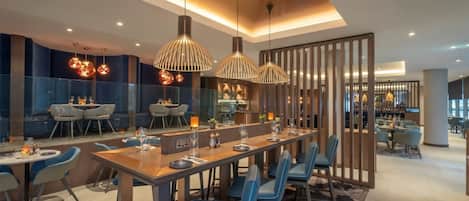 A modern dining area with a long table, blue chairs, and pendant lights.