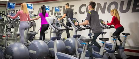 Un gimnasio con varias cintas de correr y bicicletas estáticas, un espejo grande y carteles de motivación en la pared.