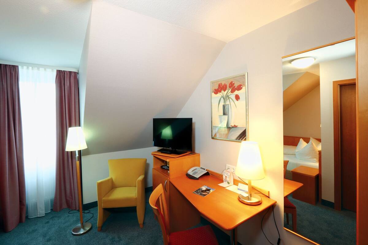 Ein Hotelzimmer mit Schreibtisch, Stuhl, Fernseher, Lampe und einem Bild an der Wand.
