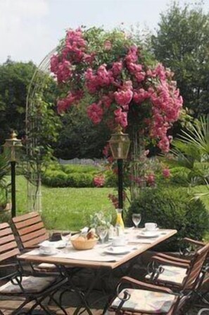 An outdoor dining area with a table set for two, surrounded by lush greenery and a flowering plant. - Hotel & Restaurant Eurohof (Duisburg)