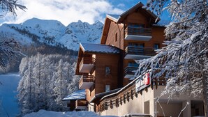 A wooden lodge with multiple balconies, surrounded by snow-covered trees and mountains. - Pierre & Vacances Residence L'Albane (Vars)