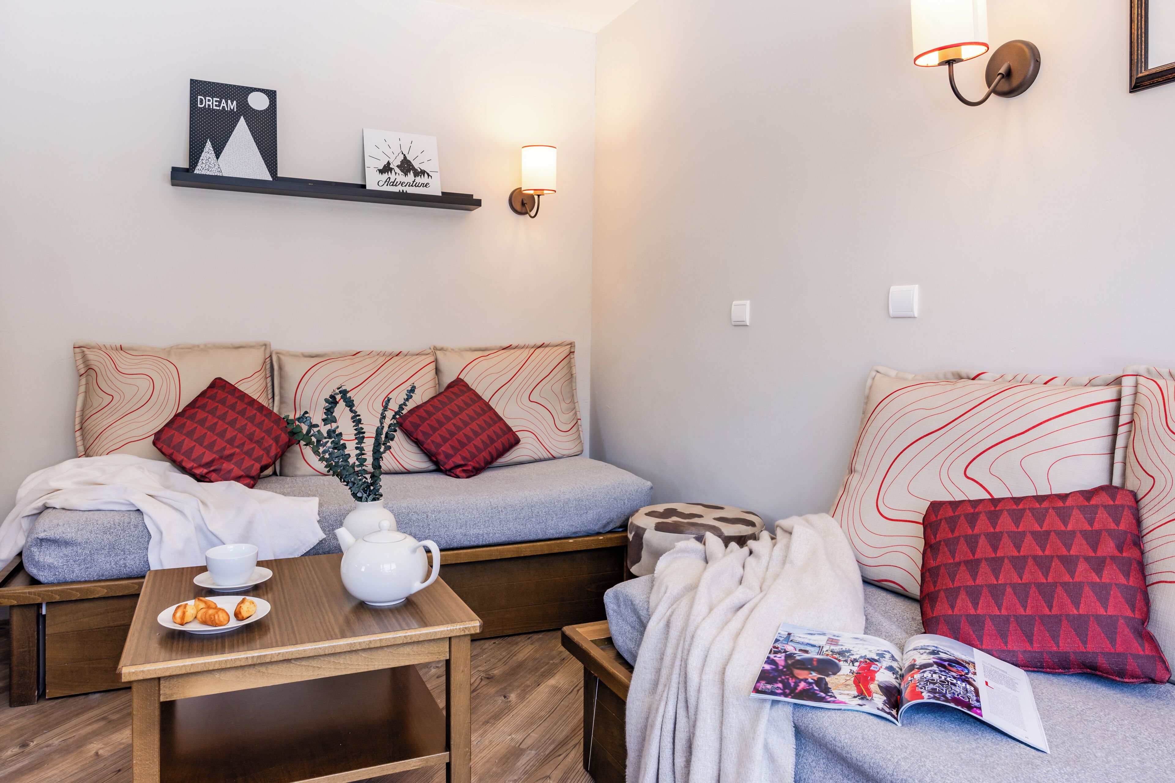 Een gezellige kamer met een bank, een klein tafeltje met een theepot, en een wandplank met decoratieve objecten.