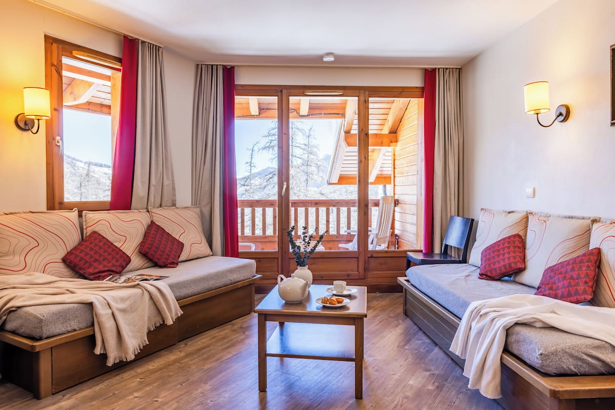 A cozy room with a sofa, a table with a teapot, and a view of a wooden deck.