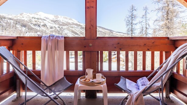 A wooden deck with two reclining chairs, a small table with a tray of food and drinks, and a view of snow-covered mountains. - Pierre & Vacances Residence L'Albane (Vars)