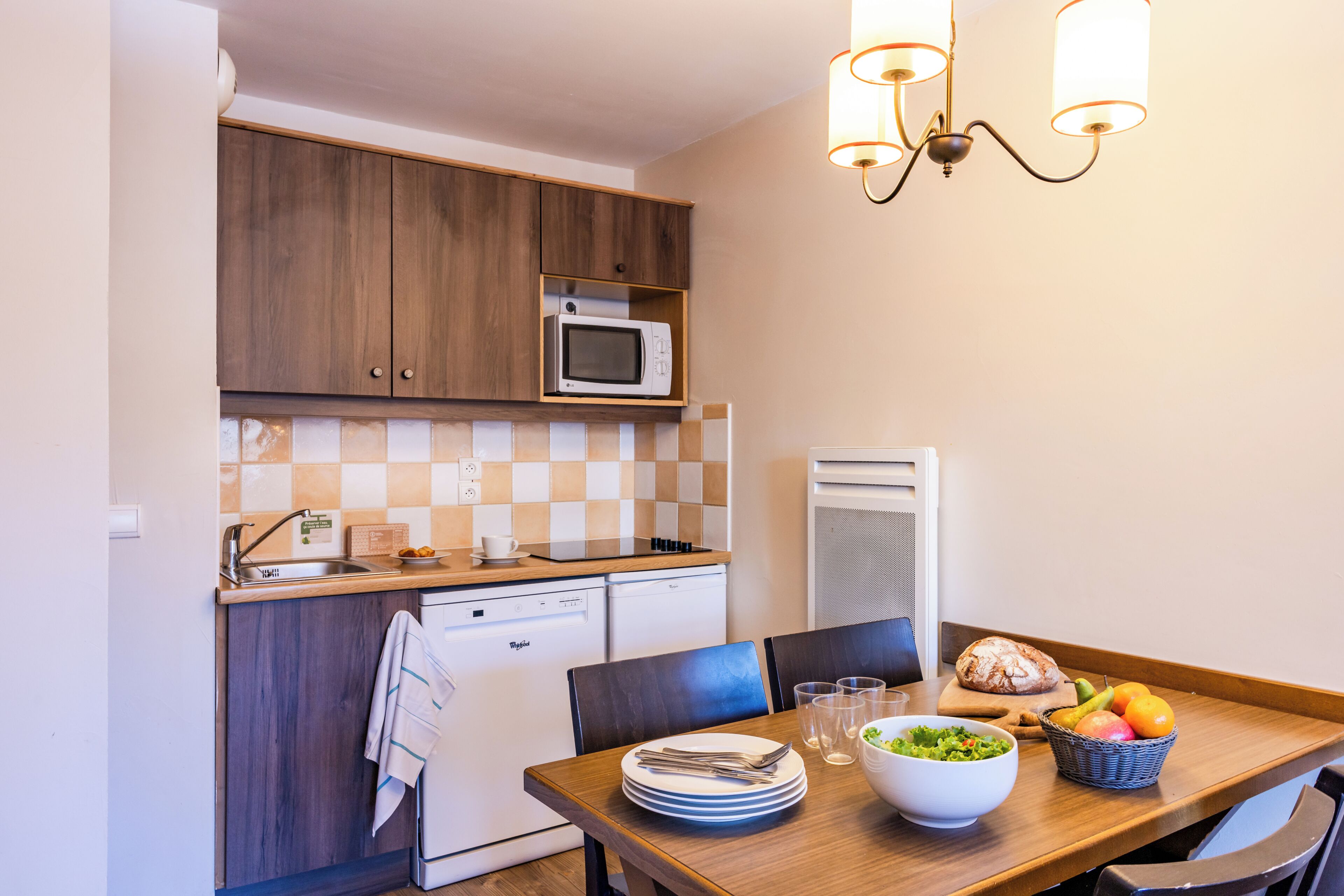 A compact kitchen with a microwave, dishwasher, and a dining area with a table set for two.