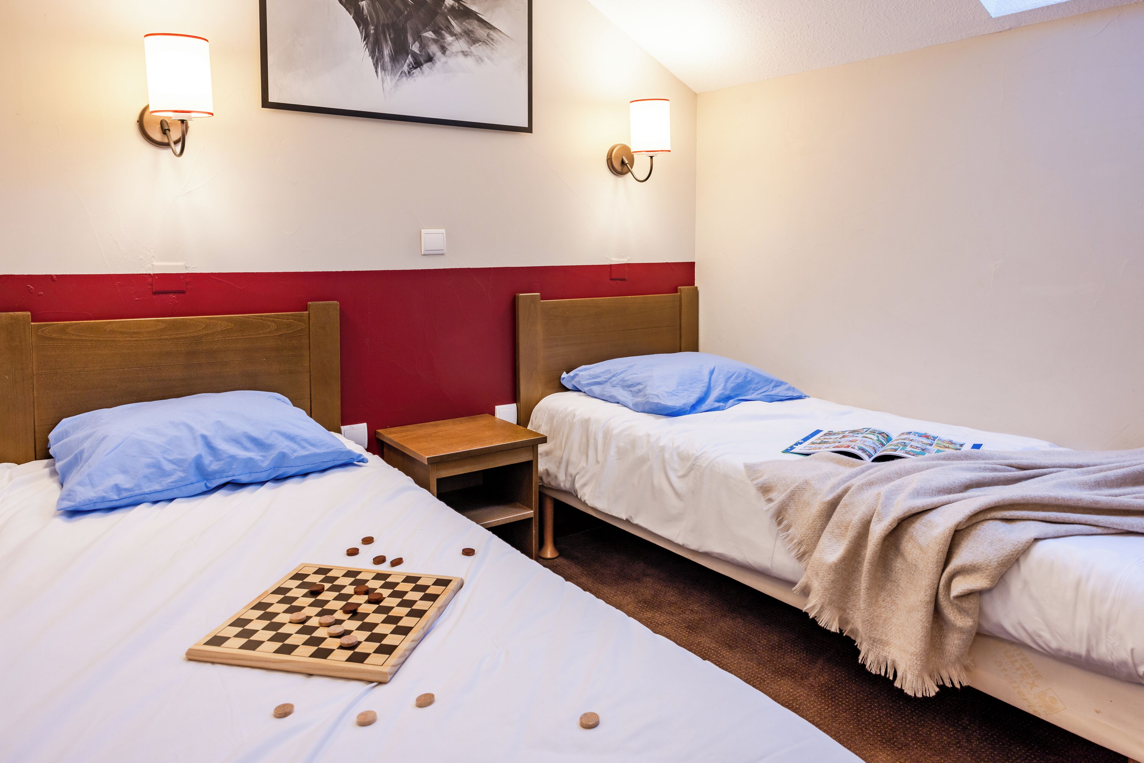 Camera d'albergo con due letti, un comodino, una scacchiera e lampade a parete.