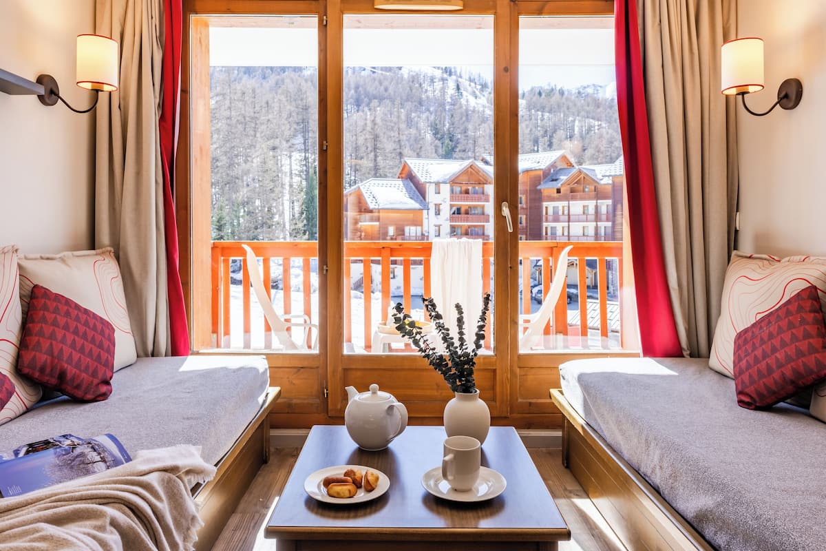 A cozy room with a wooden bed, a table with a teapot, a vase with flowers, and a plate of pastries.
