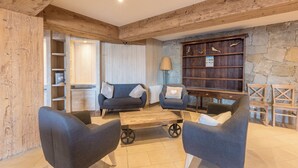 A cozy living area with a wooden ceiling, a stone wall bookshelf, and a fireplace. - Pierre & Vacances Residence L'Albane (Vars)