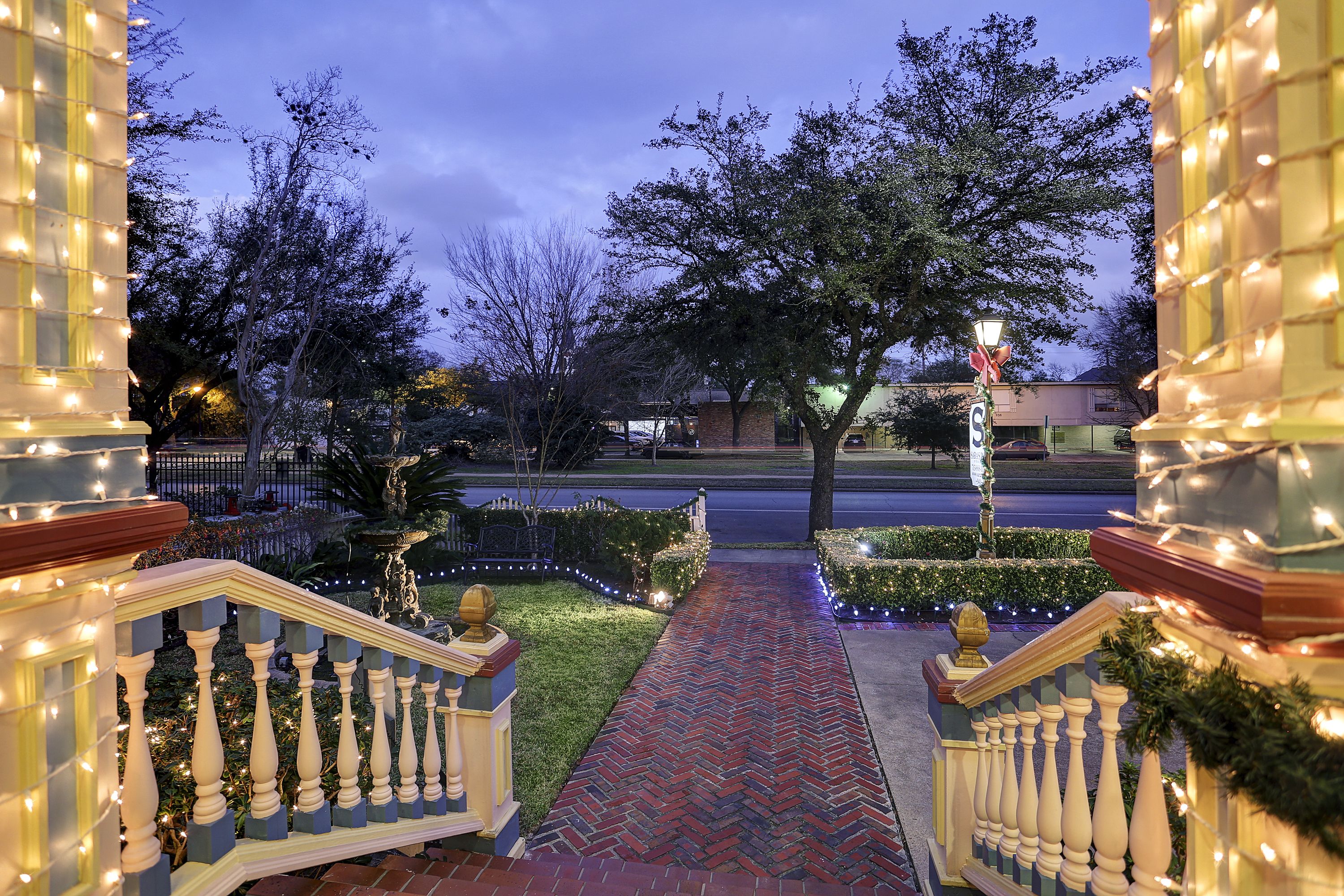 A well-lit pathway leading to a building entrance with a brick pathway, balustrades, and decorative lights.