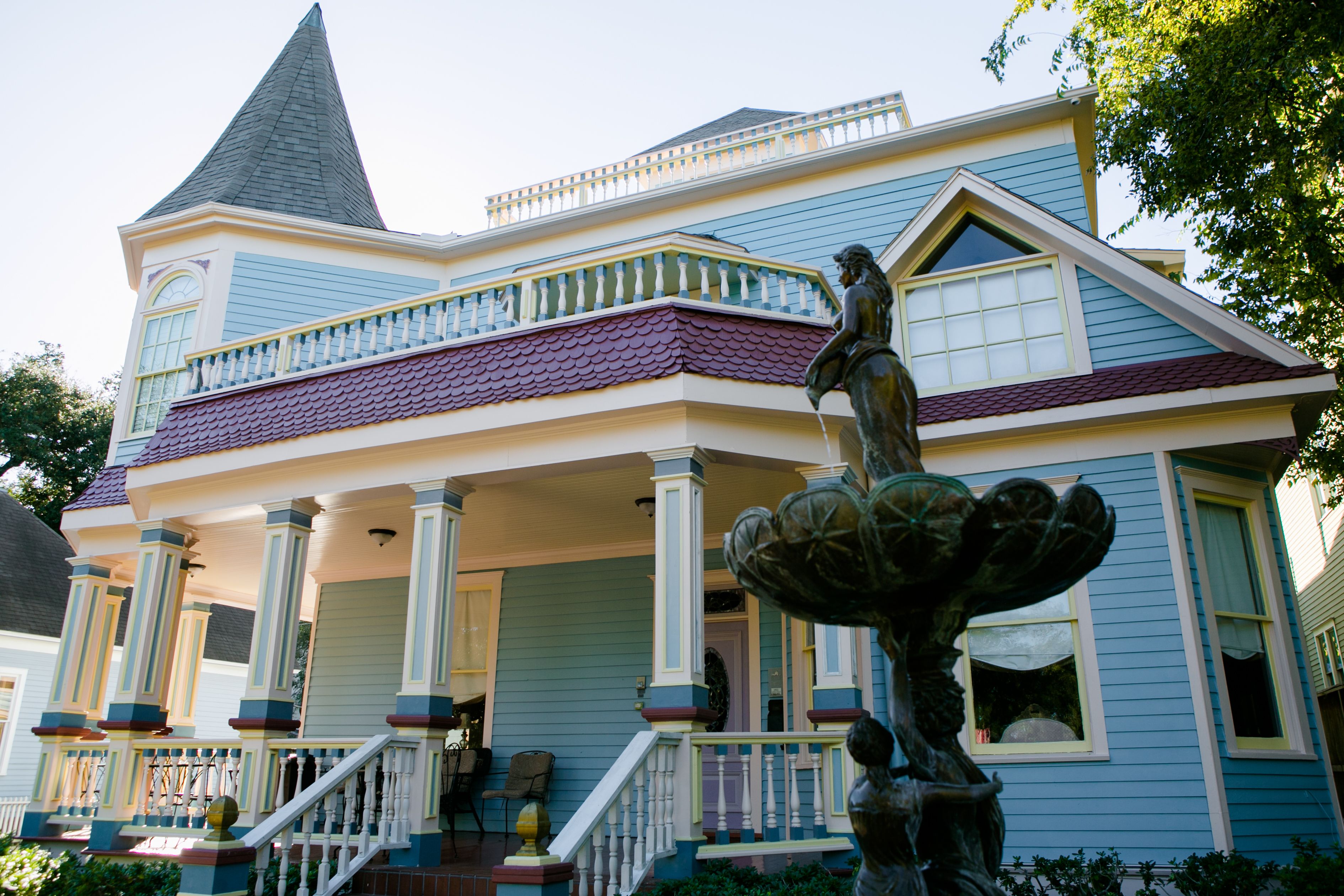 A large, two-story house with a prominent tower, a porch with columns, and a statue of a woman.