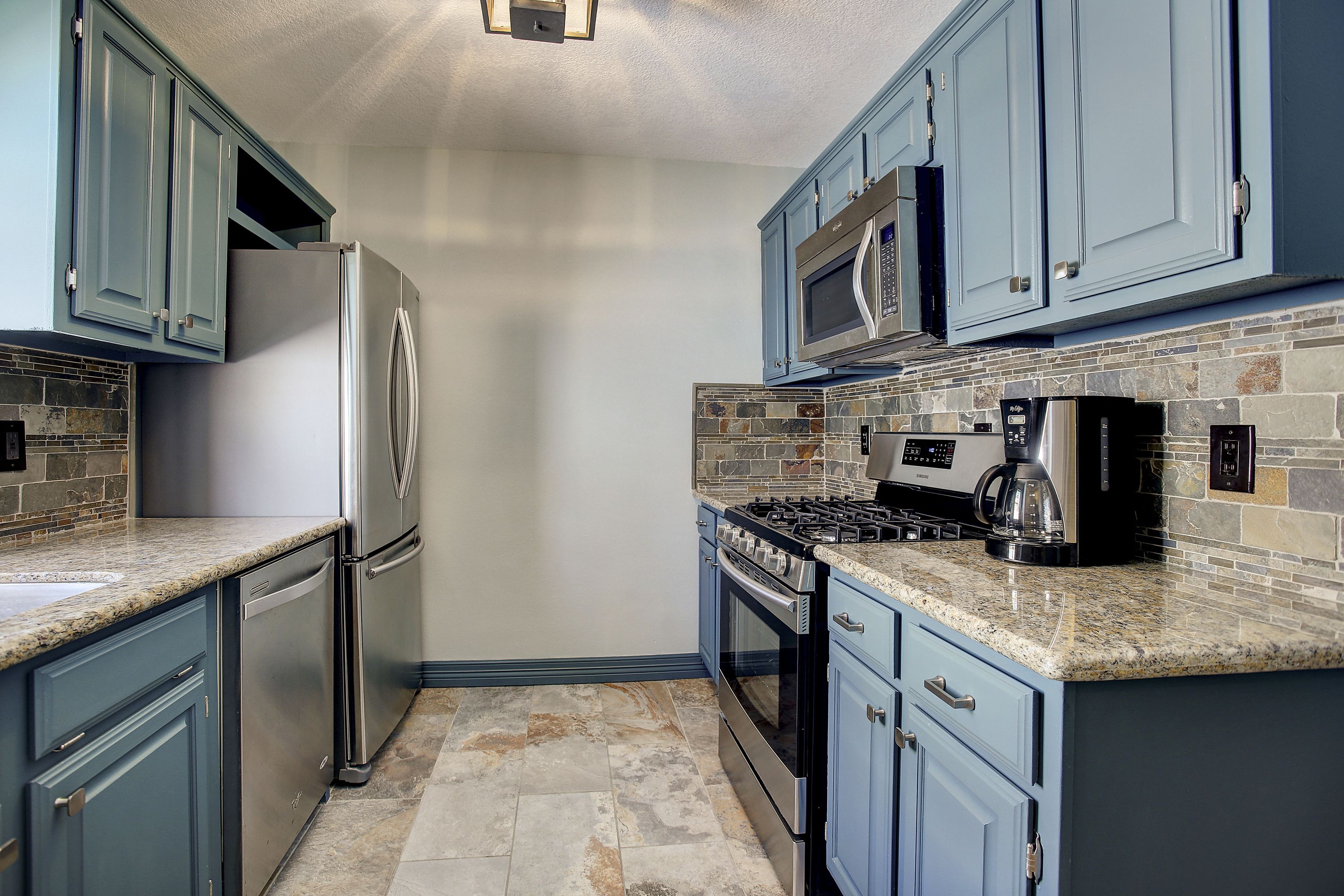 A kitchen with blue cabinets, a stainless steel refrigerator, a microwave, a stove, and a coffee maker.