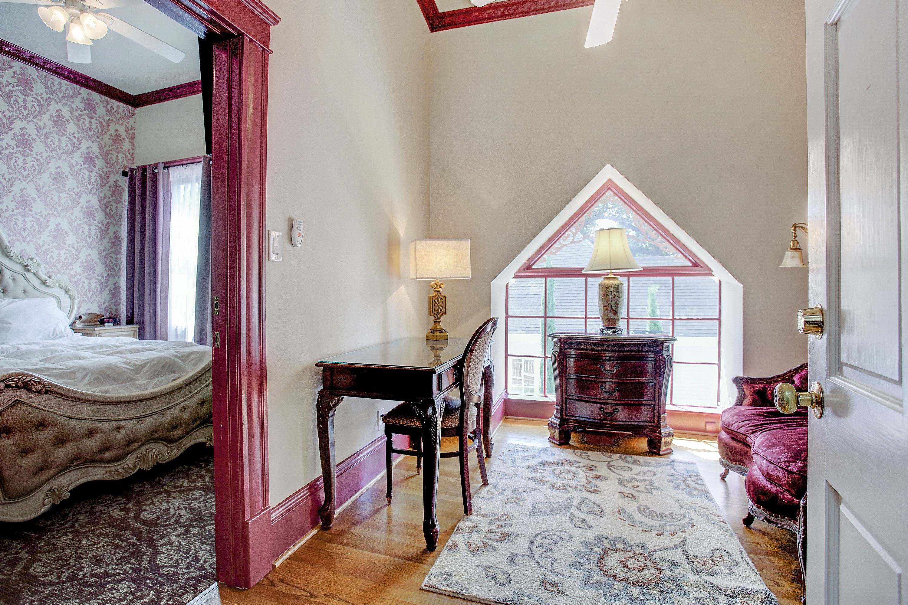 A bedroom with a large bed, a desk, and a dresser. There is a window with a view of the outside.