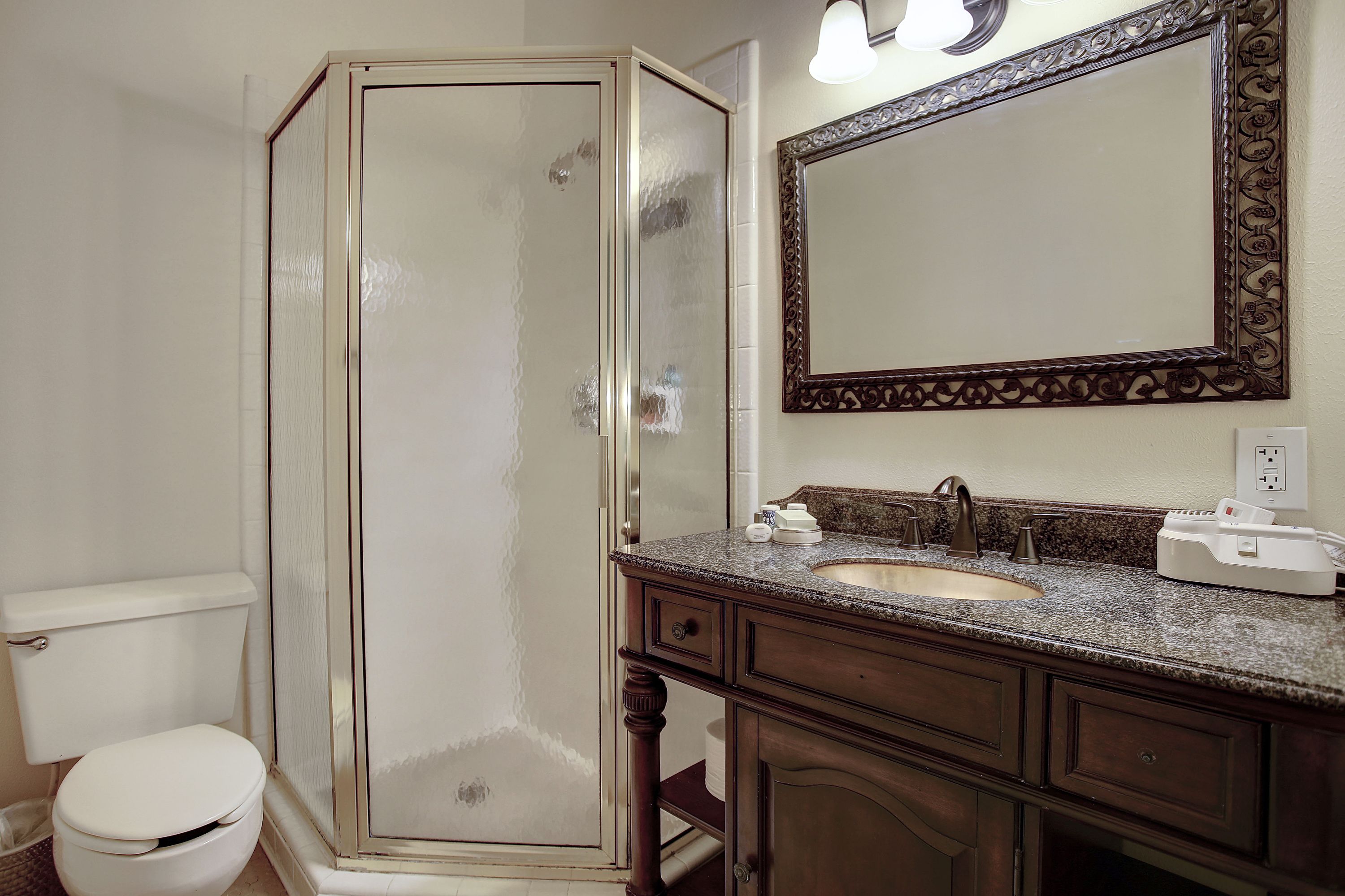 A bathroom with a glass-enclosed shower, a sink with a granite countertop, and a large mirror with an ornate frame.