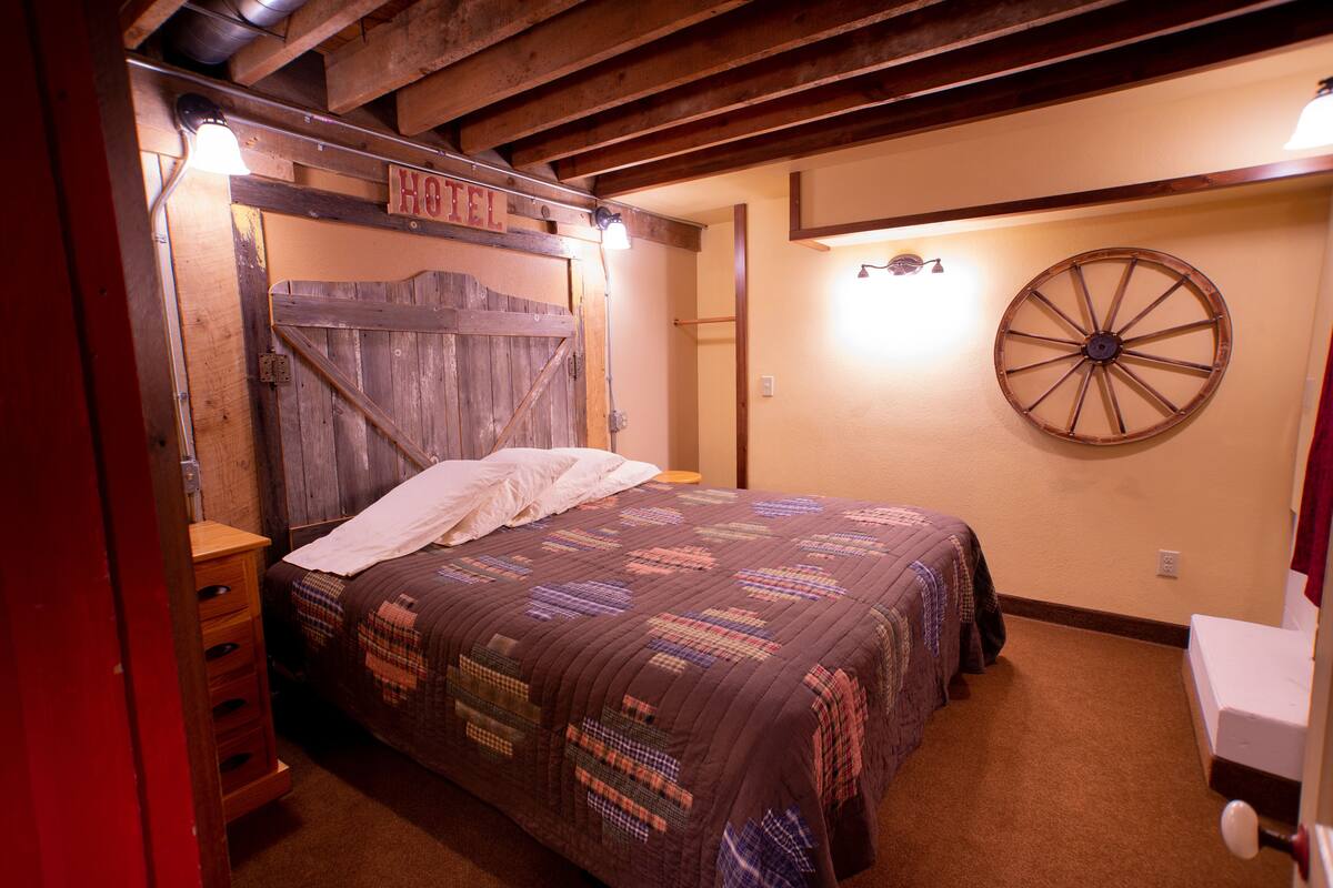 A rustic room with a wooden bed, a wooden ladder, a wheel, and a sign that reads "HOTEL".