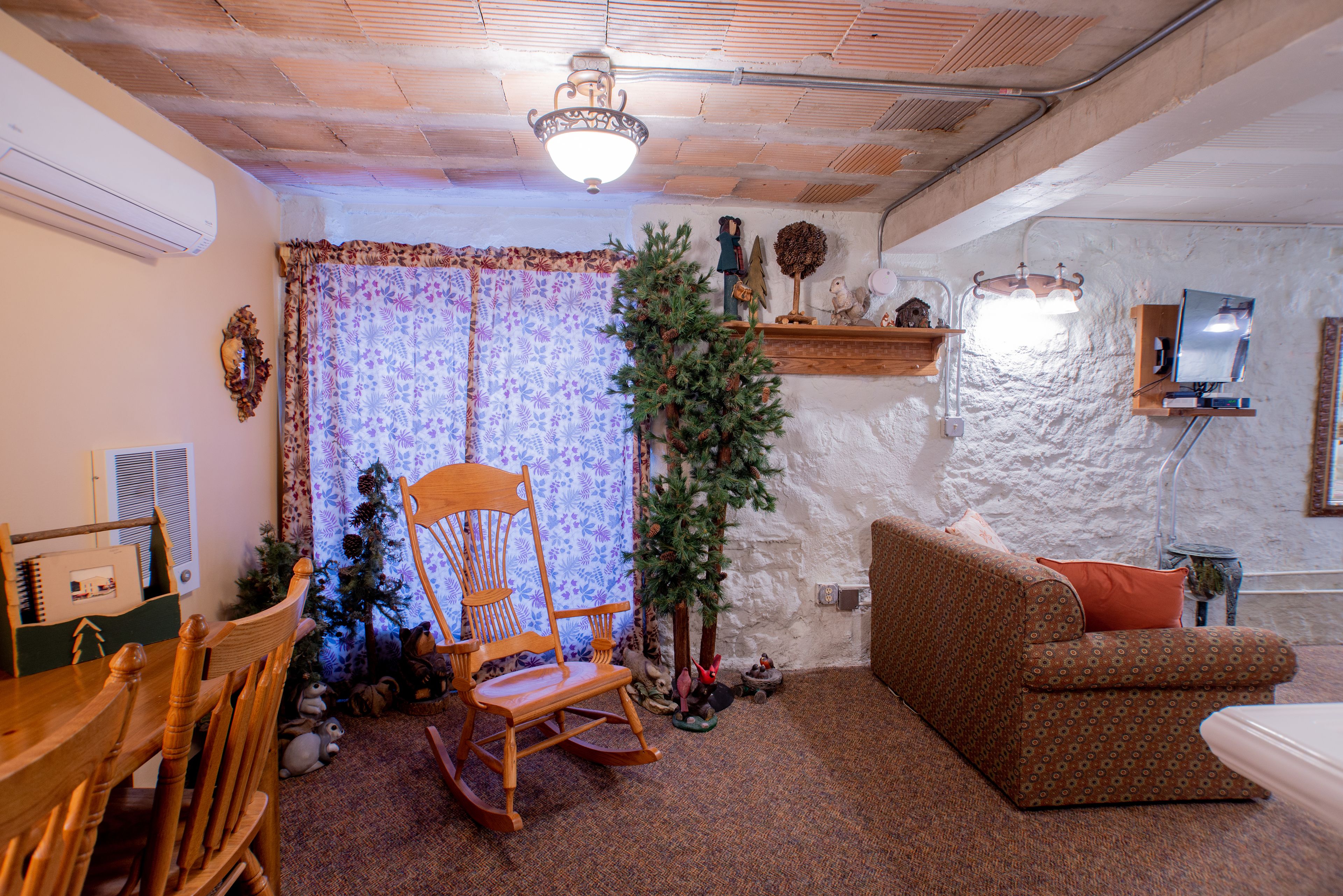 A cozy living room with a wooden rocking chair, a patterned sofa, and a small Christmas tree.