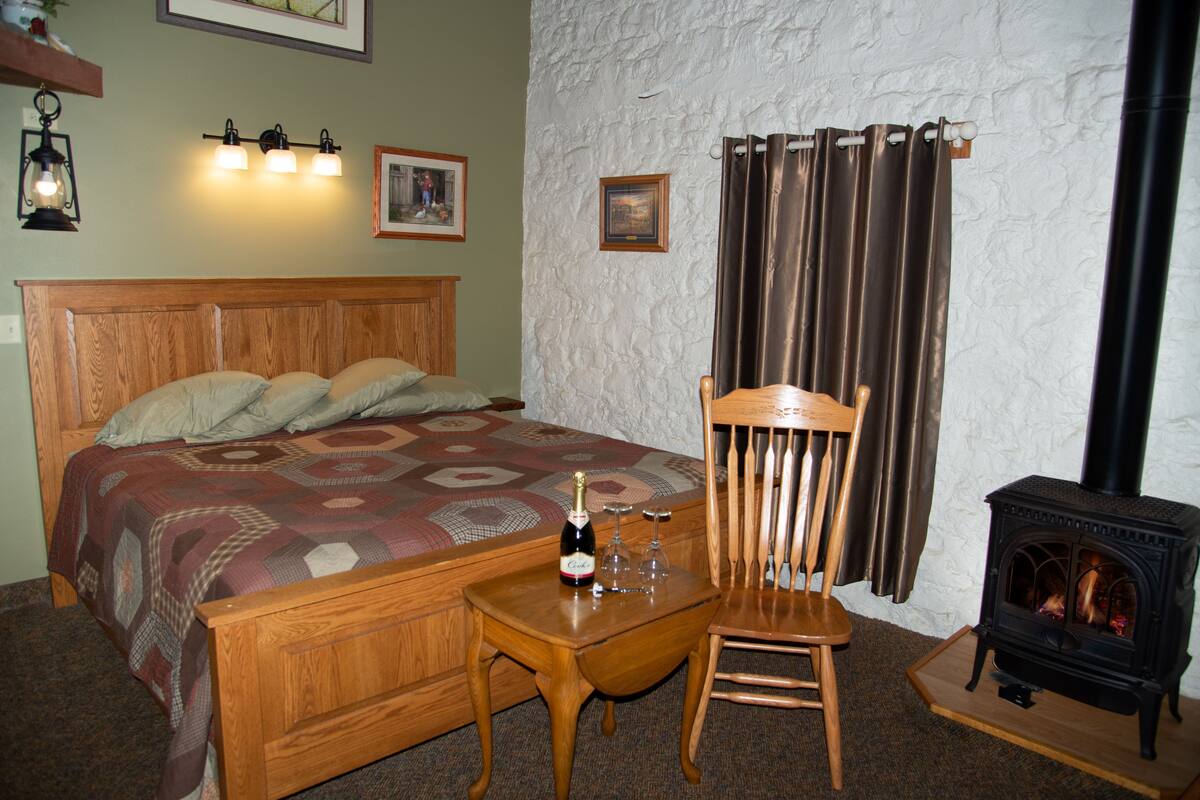 A bedroom with a wooden bed, a nightstand, a chair, a fireplace, and wall-mounted lights.