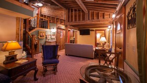 A spacious living area with a high ceiling, wooden beams, a blue armchair, a sofa, and a glass coffee table. - Stone Mill Hotel & Suites (Lanesboro)