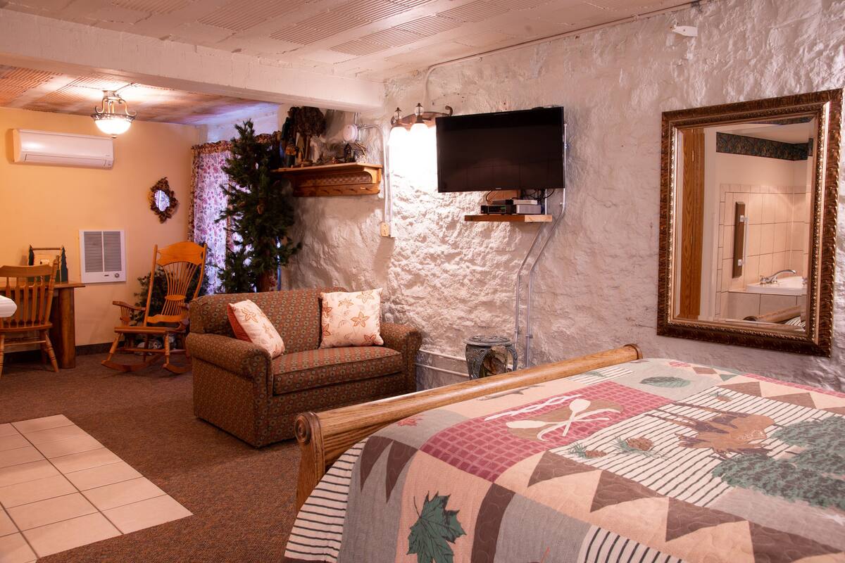 A cozy living room with a sofa, a wooden rocking chair, a television, and a large mirror.